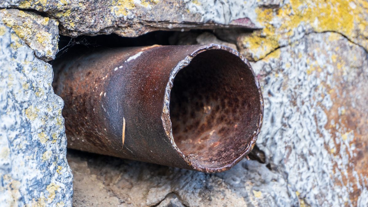 End of an old iron pipe projecting from a stone wall, its bore narrowed by rust and scale