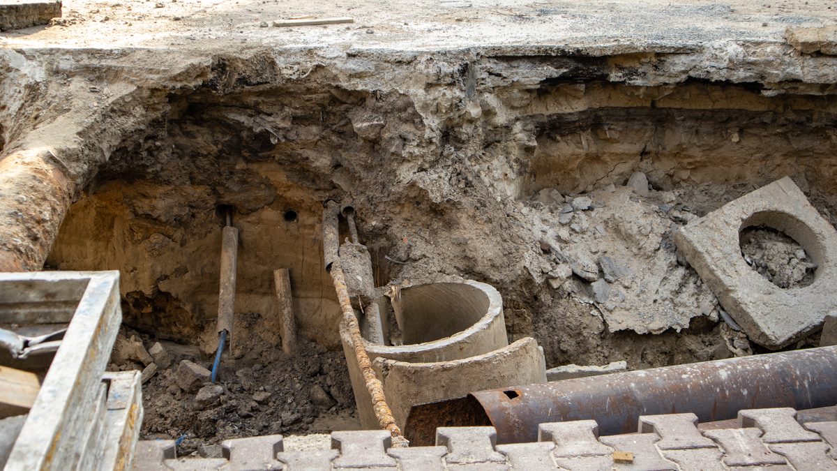 Open excavation beneath block paving, exposing a broken pipe section and the trench wall around it