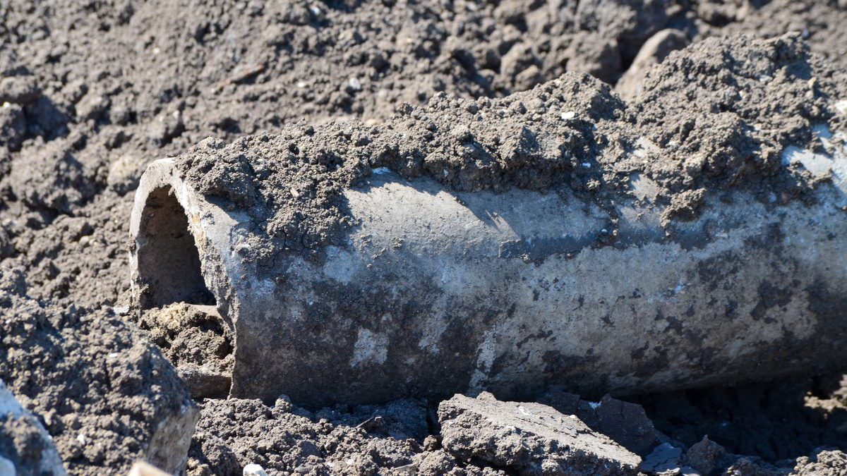 Broken section of an old buried pipe exposed in excavated soil, its open end and a loose fragment beside it